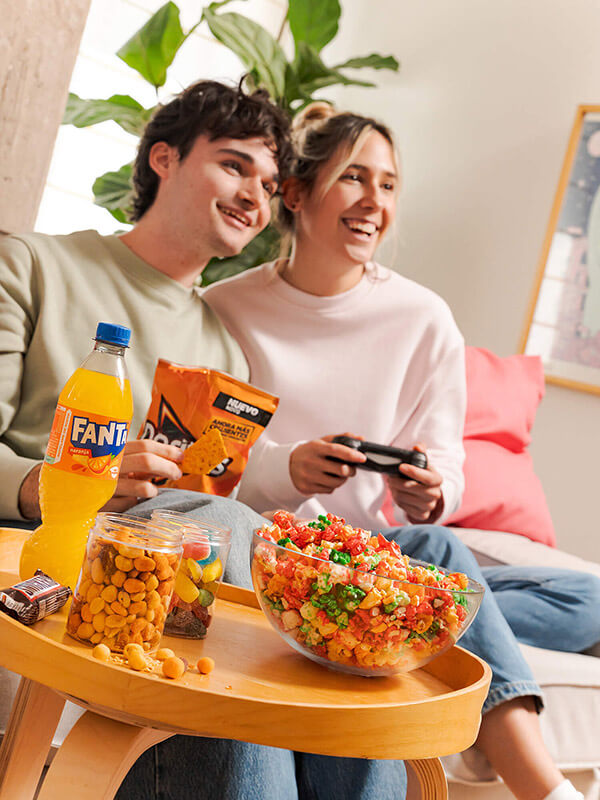 Imagen de una pareja de adolescentes jugando a la consola y comiendo dulces belros